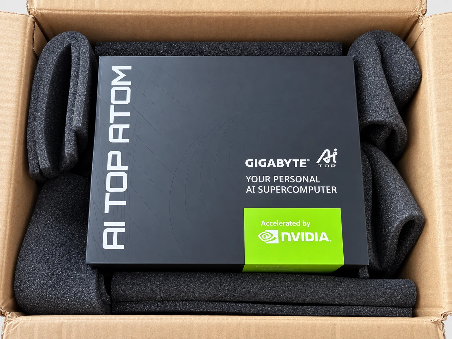輸送用の箱に入れ、緩衝材で固定されたAI TOP ATOMの黒い筐体。GIGABYTE AI TOPおよびAccelerated by NVIDIAの表記があります。